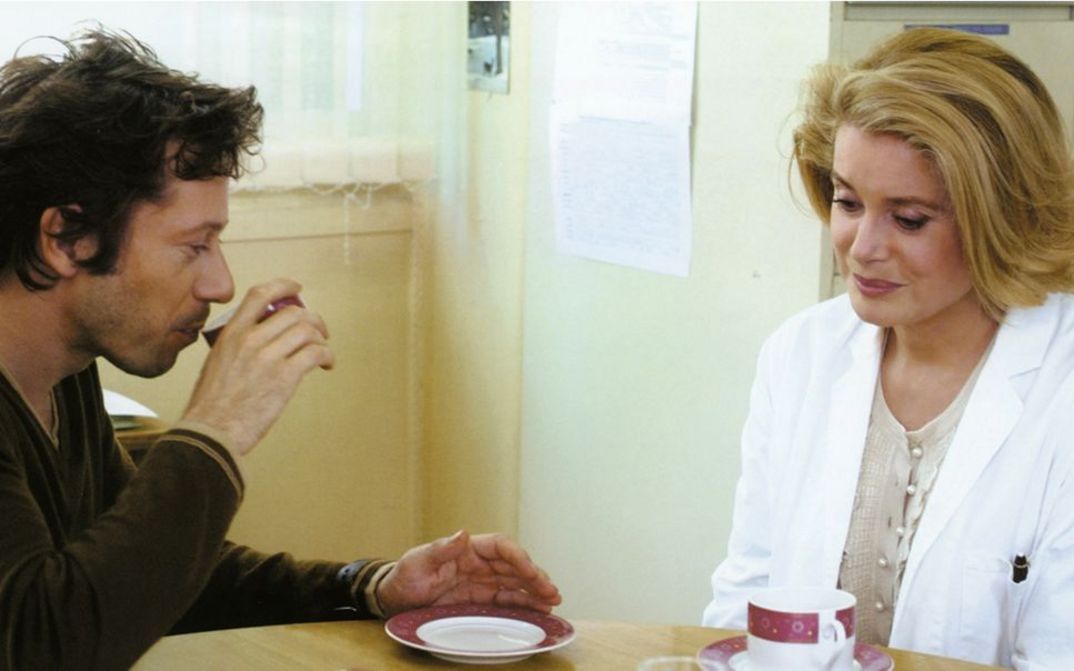 Filmstill aus ROIS ET REINE. Mathieu Amalric und Catherine Deneuve an einem Tisch, vor sich Kaffeetassen.