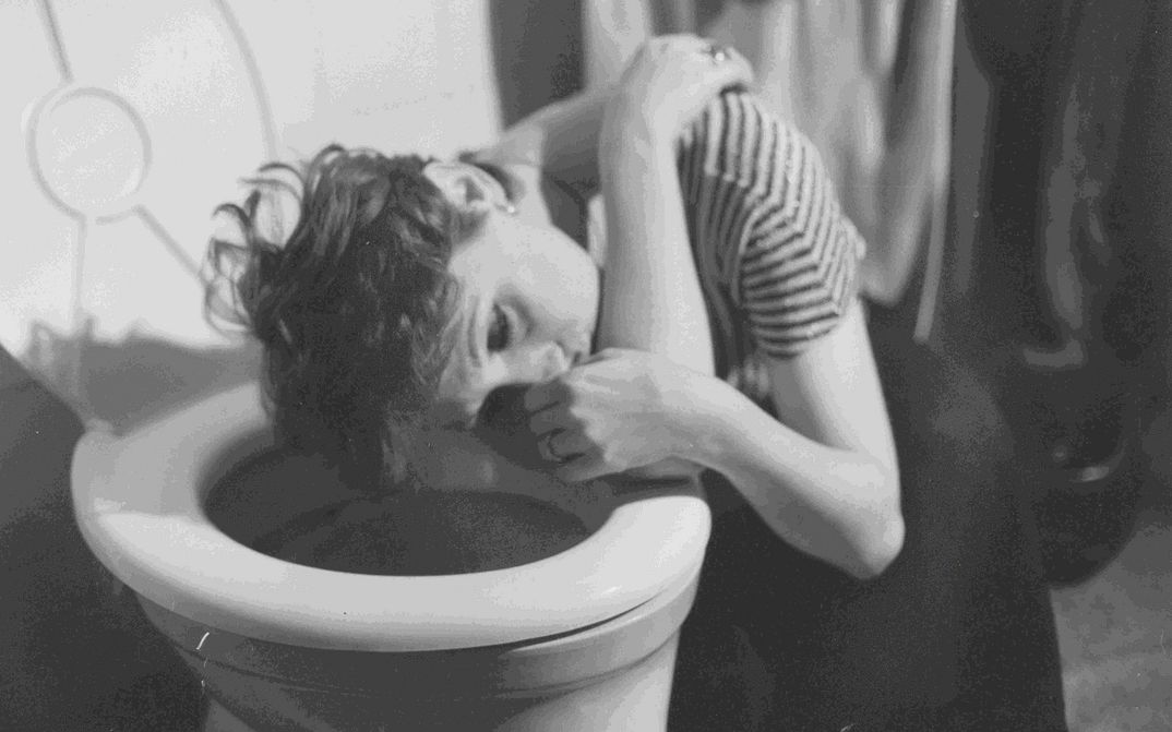 Filmstill aus EIN GANZ UND GAR VERWAHRLOSTES MÄDCHEN: Eine Frau mit kruzem Haar kauert mit dem Kopf über der Toilettenschüssel. Sie wirkt benommen.