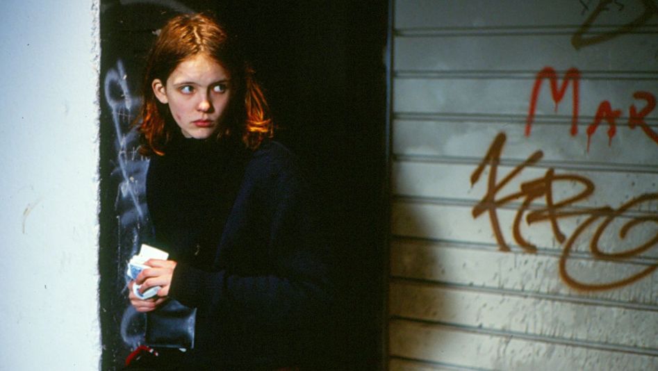 Filmstill aus OSTKREUZ: Ein junges Mädchen steht vor einer mit Graffiti bemalten Wand und blickt misstrauisch um sich.
