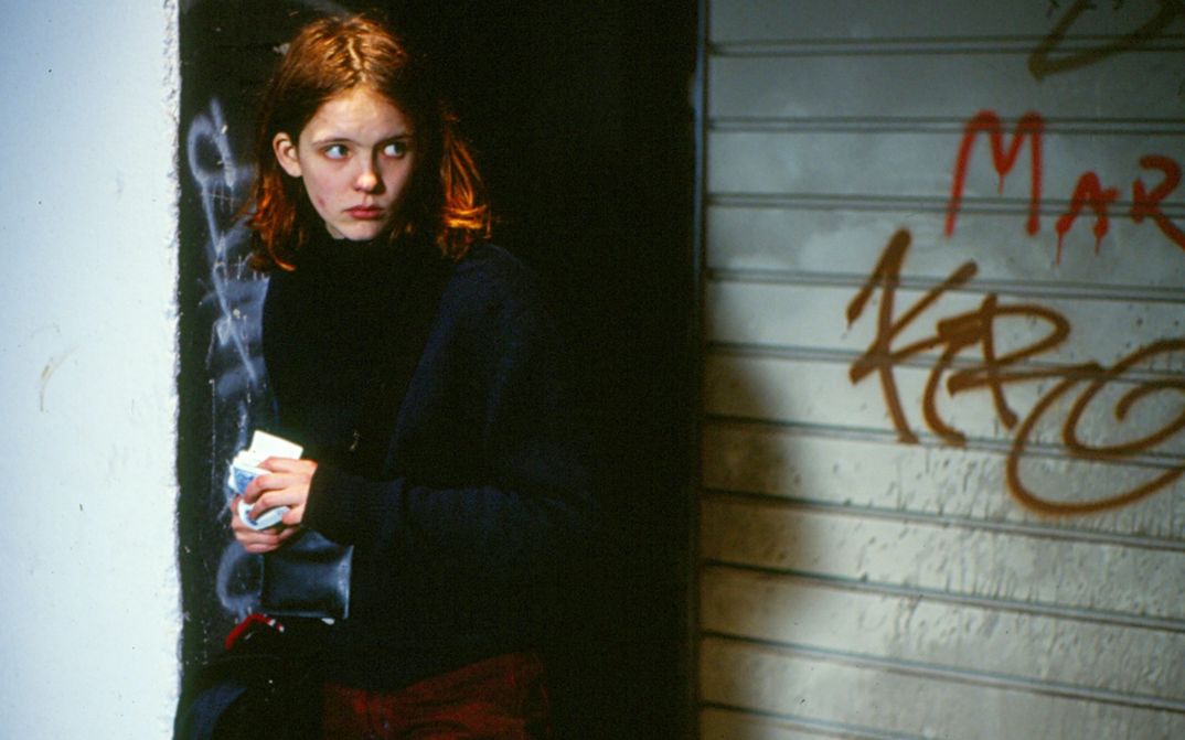 Filmstill aus OSTKREUZ: Ein junges Mädchen steht vor einer mit Graffiti bemalten Wand und blickt misstrauisch um sich.