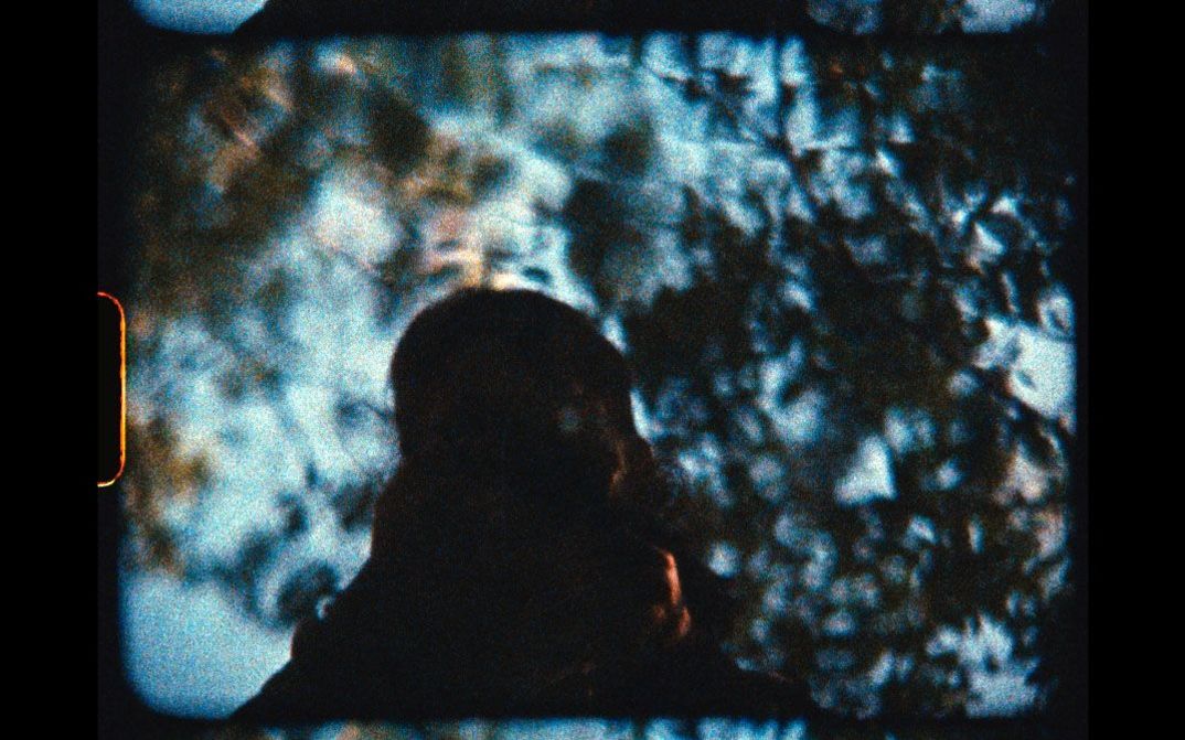 Silhouette einer Person vor unscharfen Baumkronen. Scan eines analogen Films mit Perforation.