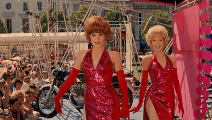 Filmstill aus LES DEMOISELLES DE ROCHEFORT: Zwei junge Frauen in roten Paillettenkleidern tanzen auf einem Volksfest.