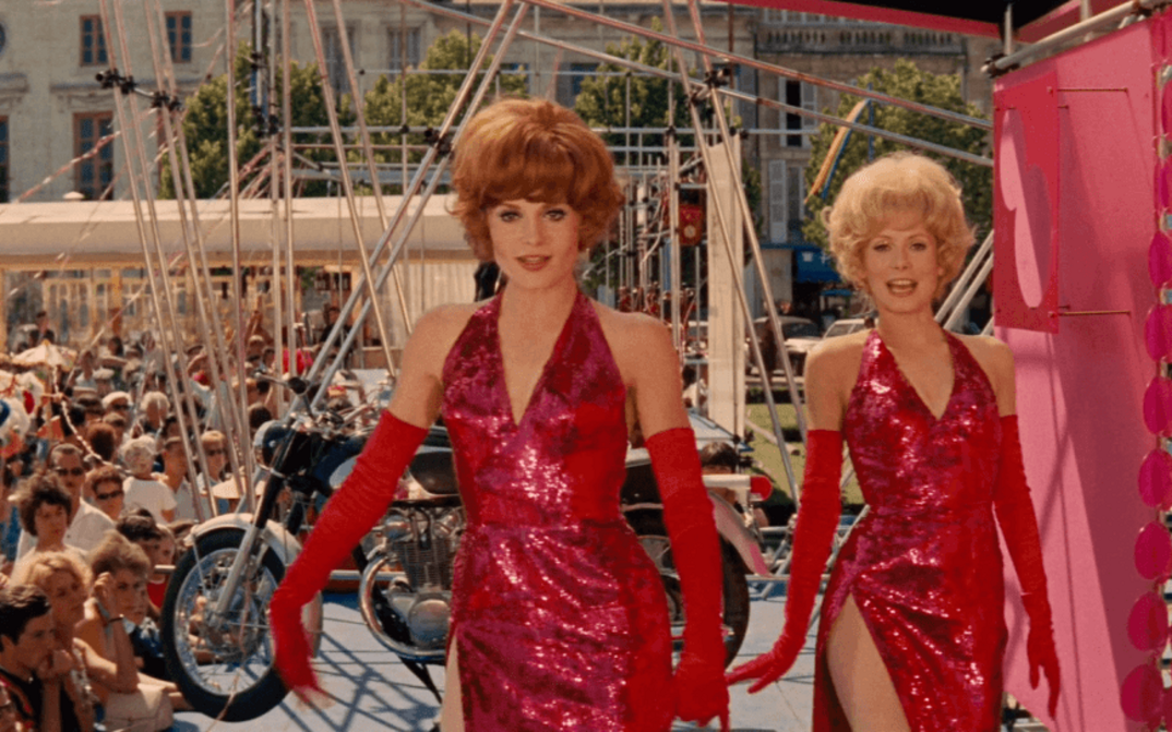 Filmstill aus LES DEMOISELLES DE ROCHEFORT: Zwei junge Frauen in roten Paillettenkleidern tanzen auf einem Volksfest.
