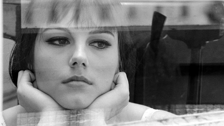 Film still from IO LA CONOSCEVO BENE: A young woman gazes thoughtfully out of the window, resting her face in her hands.