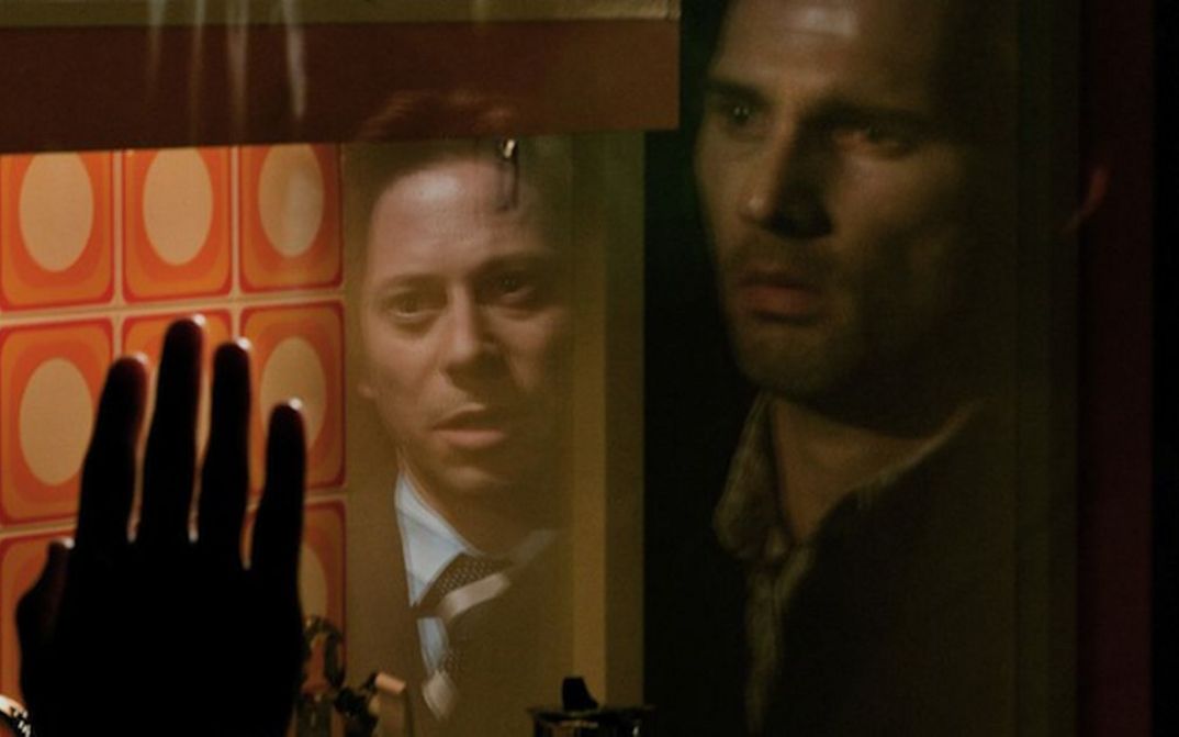 Filmstill aus MUNICH. Zwei Männer in einer Glasscheibe gespiegelt.