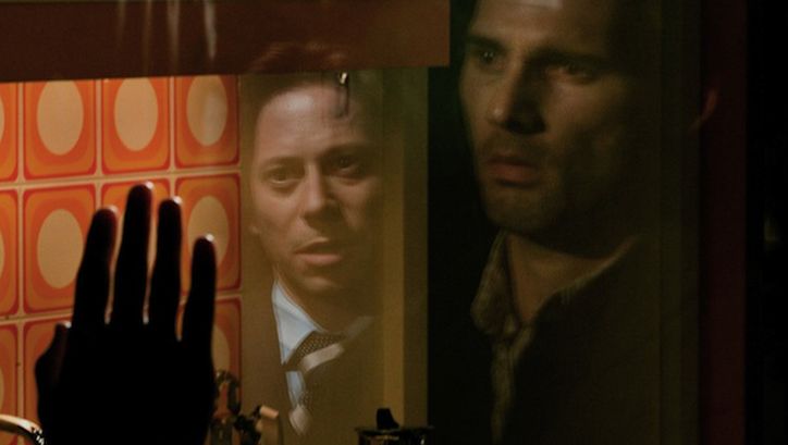 Filmstill aus MUNICH. Zwei Männer in einer Glasscheibe gespiegelt.