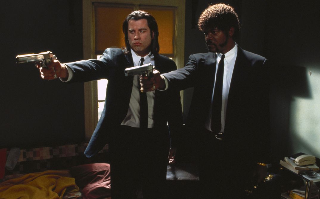 Film still from PULP FICTION: Two men in suits and ties stand side by side, pointing their guns at something outside the frame.