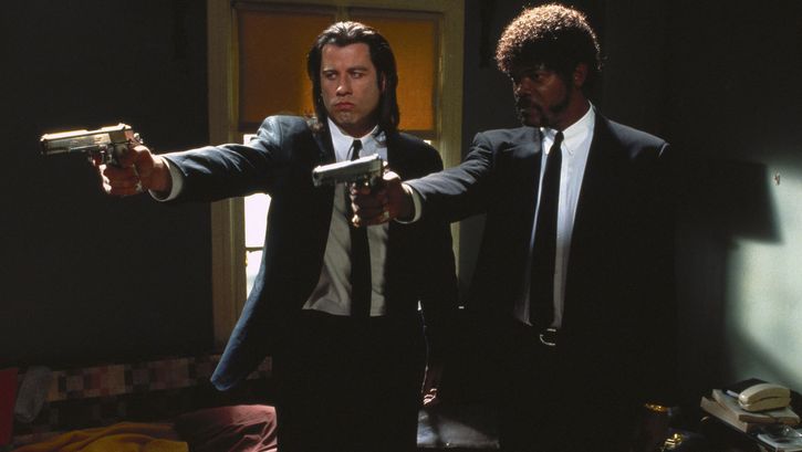 Film still from PULP FICTION: Two men in suits and ties stand side by side, pointing their guns at something outside the frame.