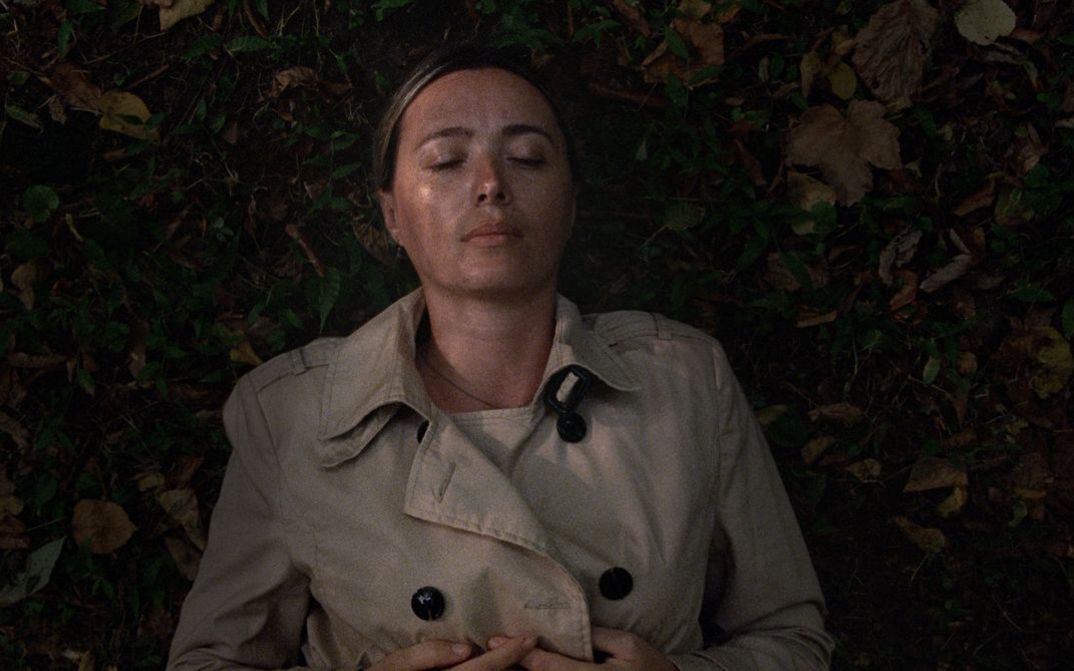 Filmstill aus BEGINNING. Eine Frau liegt mit geschlossenen Augen im Gras.