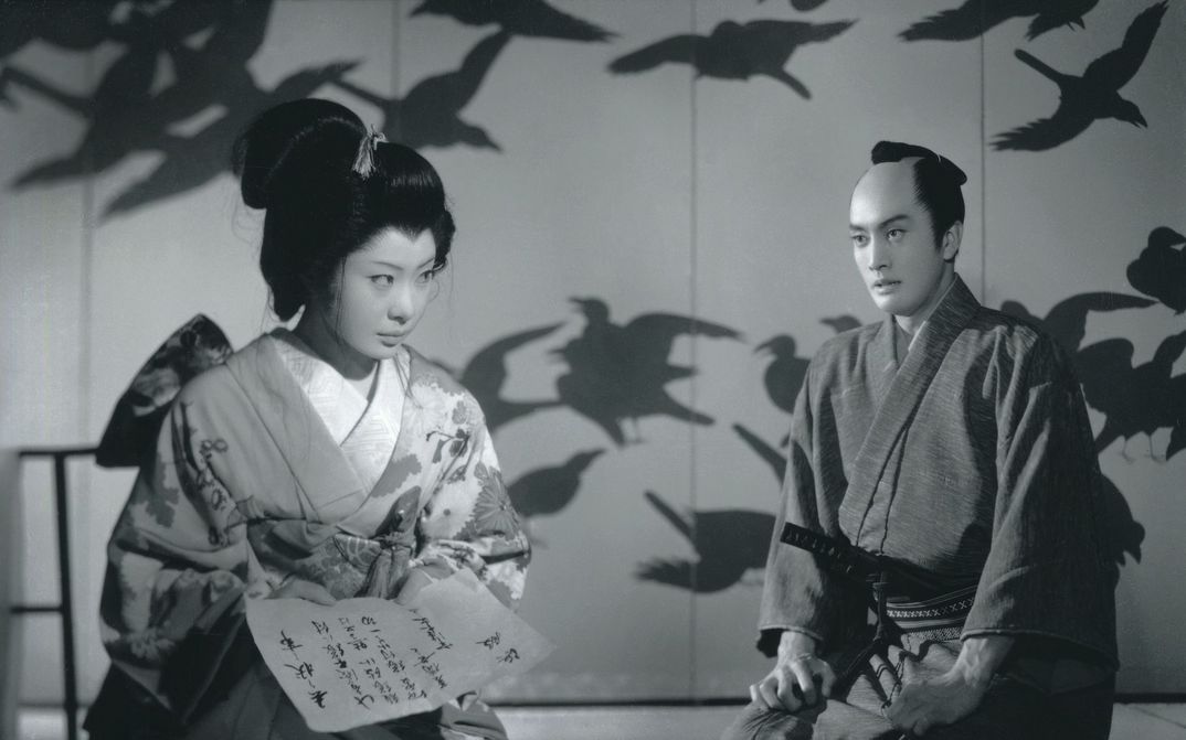 Film still from SWORD OF DOOM: A man and a woman in traditional Japanese kimonos are sitting in a room. The wall behind them is painted with birds.