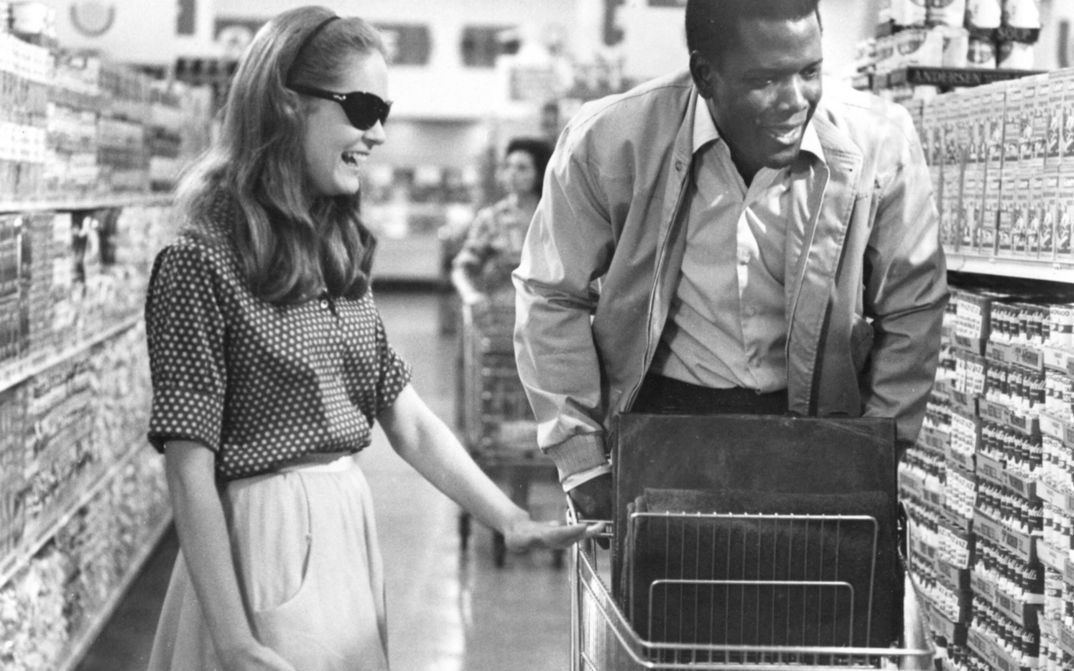Filmstill aus A PATCH OF BLUE: Ein Mann und eine Frau beim Einkaufen im Supermarkt. Beide lachen, sie trägt eine dunkle Brille. 
