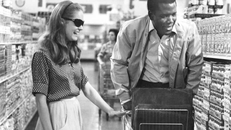 Filmstill aus A PATCH OF BLUE: Ein Mann und eine Frau beim Einkaufen im Supermarkt. Beide lachen, sie trägt eine dunkle Brille. 