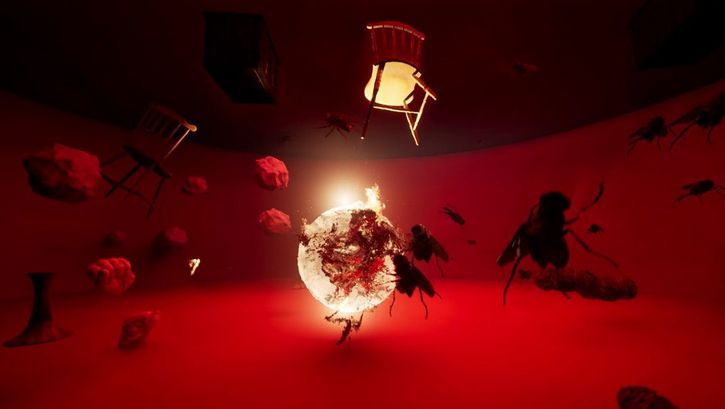 Filmstill aus dem Film „Simia: Stratagem for Undestining" von Assem Hendawi. Ein runder, niedriger Raum in rotem Licht. In der Mitte ein glühender Feuerball, um ihn herum fliegende Gegenstände (Steine, Stühle), eine Hand und Insekten.