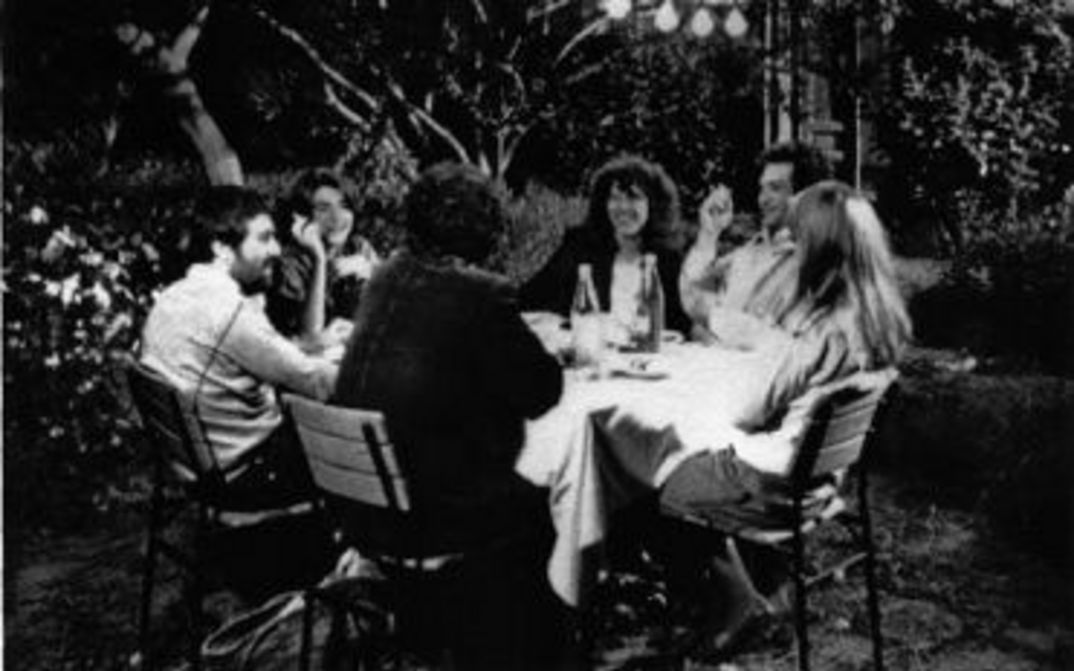 Film still from TEKERLEME: Happy-looking people sitting around a table in a garden.