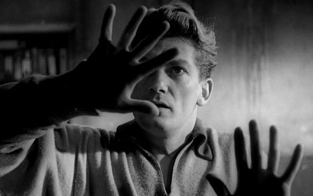 Film still from ORPHÉE: A man feels a pane of glass in front of him with his hands.