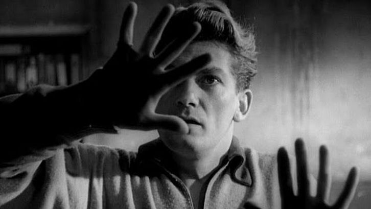 Film still from ORPHÉE: A man feels a pane of glass in front of him with his hands.