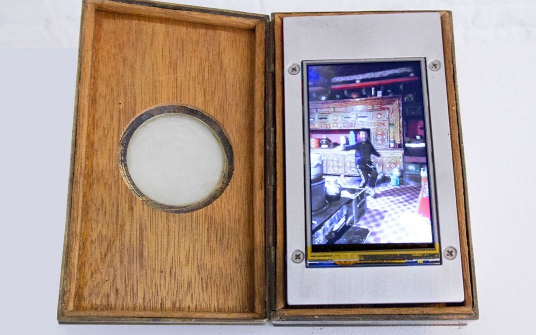 Installation view of Tenzin Phuntsog’s „Dancing Boy“. An opened box with a screen inside. On the screen a child in a kitchen.