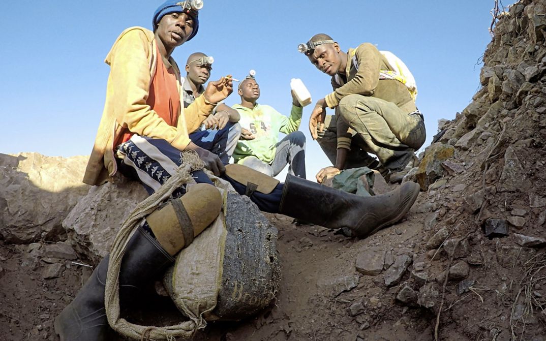 Still from the film "The Zama Zama Project" by Rosalind Morris. People with headlamps sit on the dirt floor.