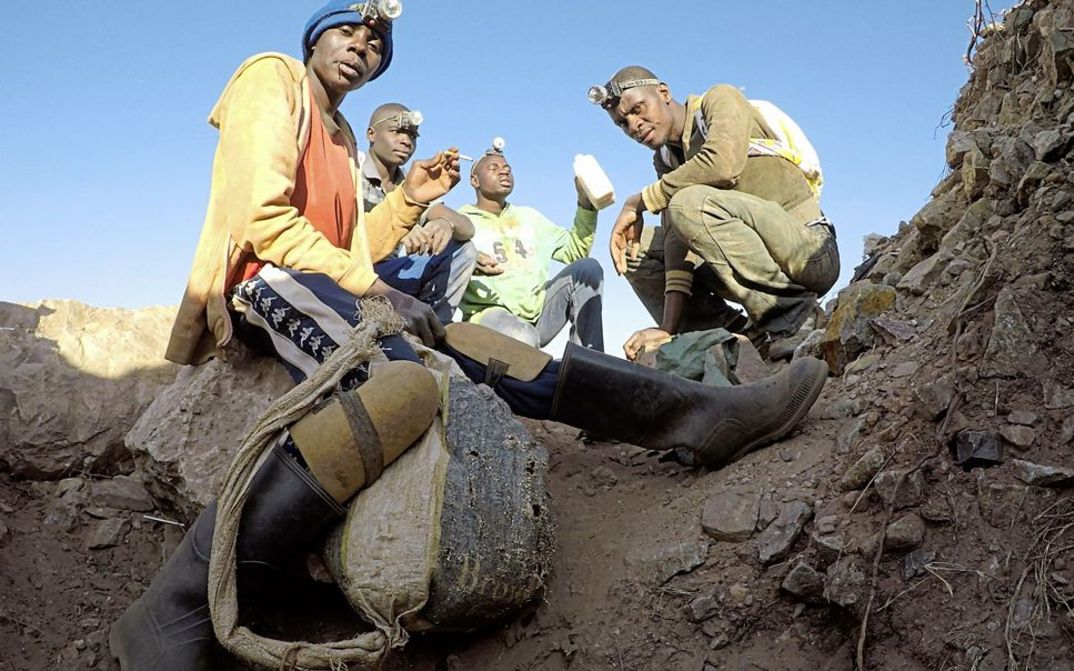 Still from the film "The Zama Zama Project" by Rosalind Morris. People with headlamps sit on the dirt floor.