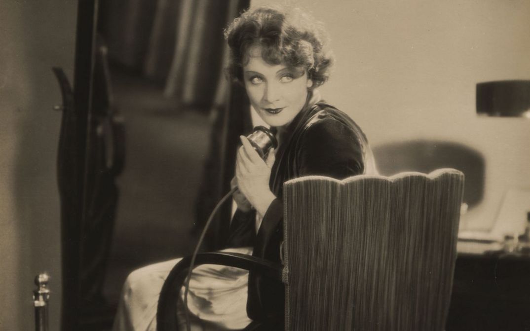 Filmstill aus DIE FRAU, NACH DER MAN SICH SEHNT. Marlene Dietrich sitzt in eleganter Kleidung auf einem Stuhl und hält ein Telefon in der Hand.