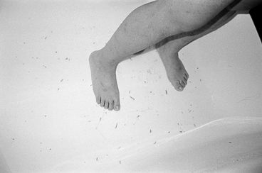 Still from the film "Jet Lag" by Zheng Lu Xinyuan. A black-and-white image of two legs standing against a grey background, photographed looking down. 