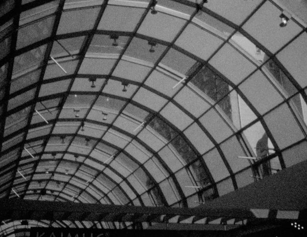Filmstill aus „This Makes Me Want to Predict the Past“ von Cana Bilir-Meier. Das geschwungene Glasdach eines Bahnhofs. 