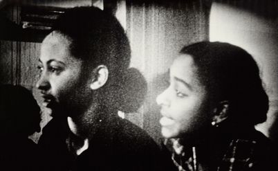 Black and white picture of two young women. You can see their left side profile. The young woman in the front is speaking. 