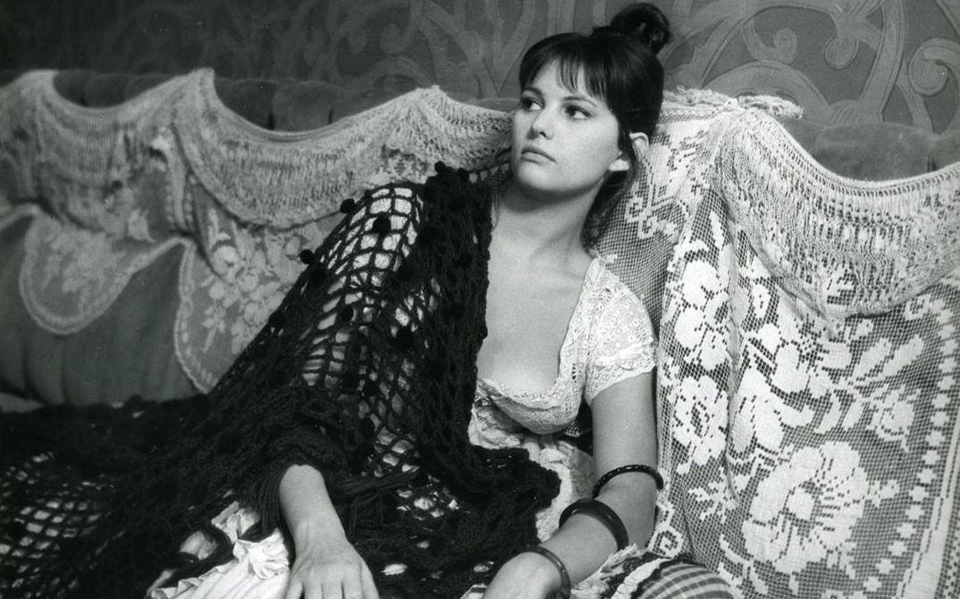 Film still from LA VIACCIA: A woman sits on a sofa.