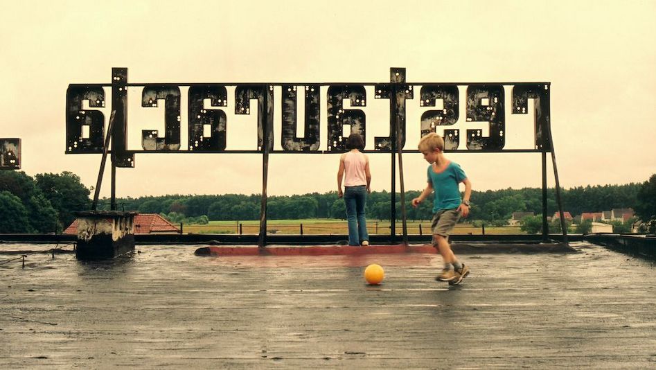Filmstill aus MILCHWALD: Zwei Kinder spielen Fußball auf einem Flachdach. Am Rande des Dachs ist von hinten der Schriftzug "Restauracja" zu sehen.