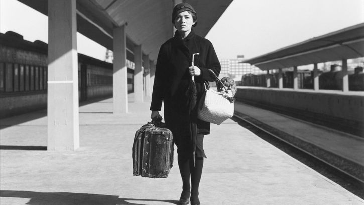 Film still from DIAS DE OTOÑO: A woman with luggage stands alone on a station platform.