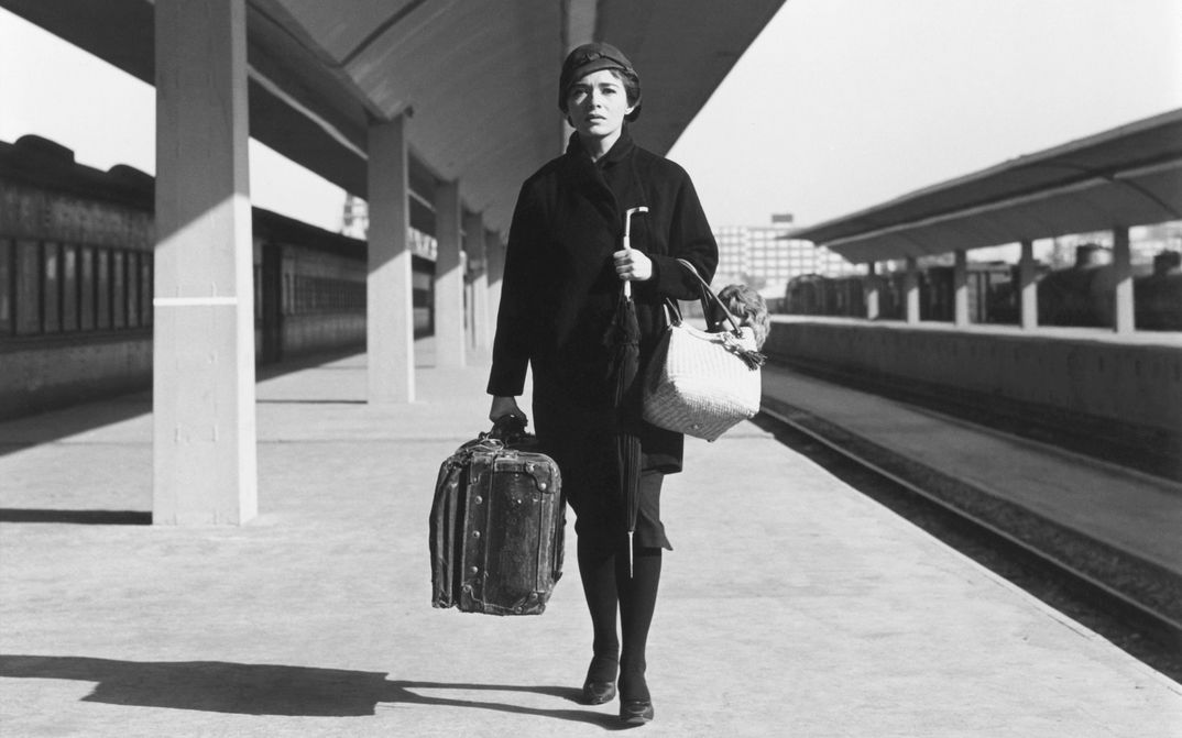 Filmstill aus DIAS DE OTOÑO: Eine Frau mit Gepäck steht alleine auf einem Bahnsteig.