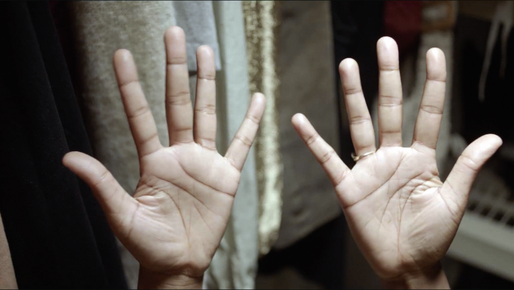 Film still from THE TUBA THIEVES: You can see the palms of two hands held in the air. 
