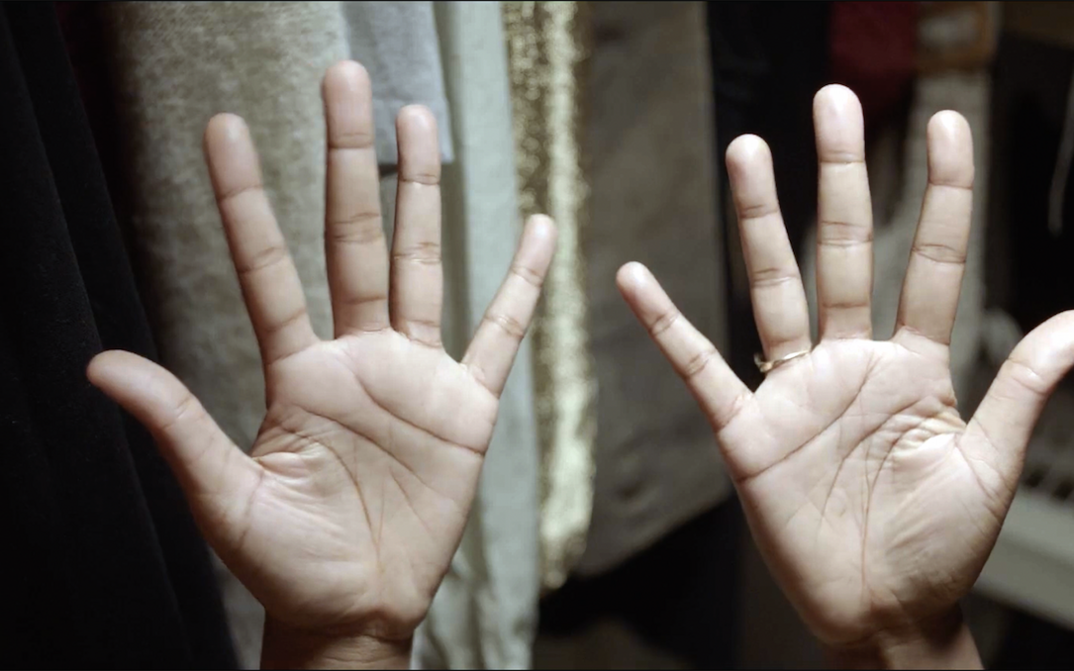 Film still from THE TUBA THIEVES: You can see the palms of two hands held in the air. 