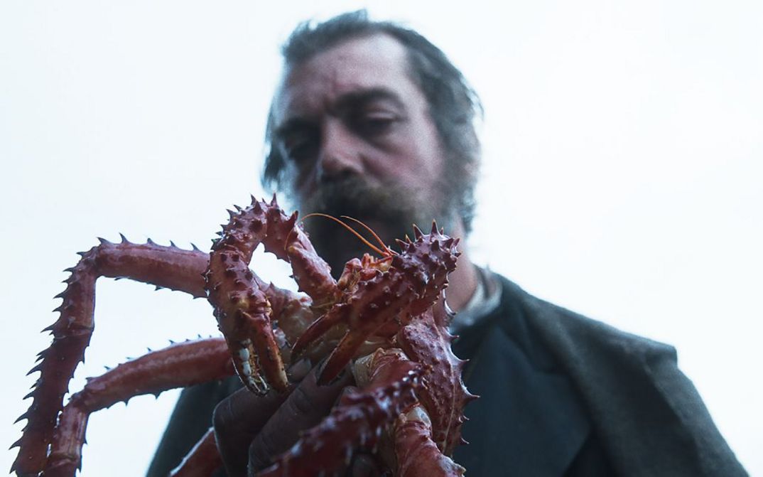 Film still from RE GRANCHIO. A man holds a king crab in his hand, his face is blurry in the background.