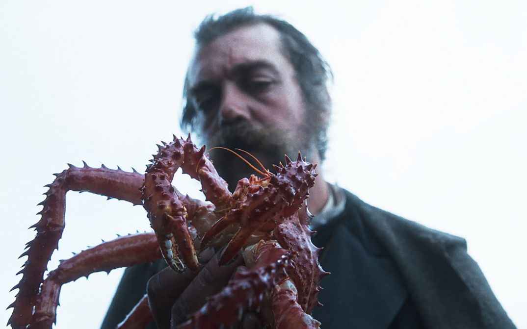 Filmstill aus RE GRANCHIO. Ein Mann hält eine Königskrabbe in der Hand, sein Gesicht ist unscharf im Hintergrund.