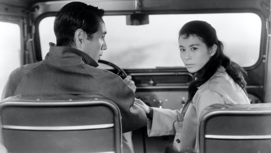 Filmstill aus ELEGY OF THE NORTH: Ein Mann und eine Frau sitzen in einem Auto, er ist am Steuer. Sie dreht sich nach hinten um, er sieht sie an.