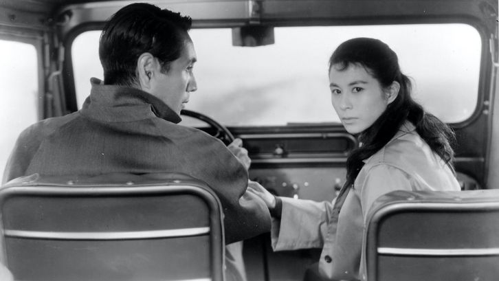 Filmstill aus ELEGY OF THE NORTH: Ein Mann und eine Frau sitzen in einem Auto, er ist am Steuer. Sie dreht sich nach hinten um, er sieht sie an.