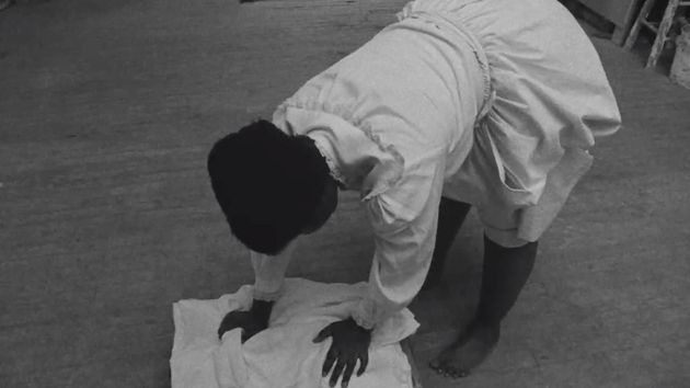 Filmstill aus dem Film „Conspiracy“ von Simone Leigh, Madeleine Hunt-Ehrlich: eine weißgekleidete Frau beugt sich über ein Stück weißen Stoffes, um diesen zu waschen.