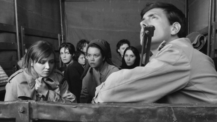 Filmstill aus LE SOLDATESSE: Mehrere Frauen mit verschrecktem Gesichtsausdruck sitzen auf einem Lastwagen. Im Vordergrund ist ein Soldat mit Gewehr.