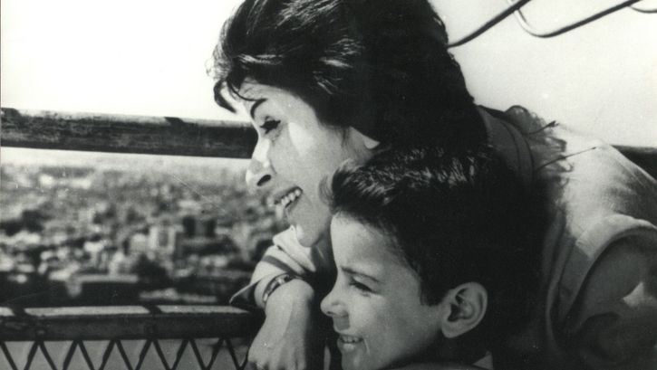 Film still from DAWN OF A NEW DAY: A woman and a boy stand close together on a roof and look out over the city.