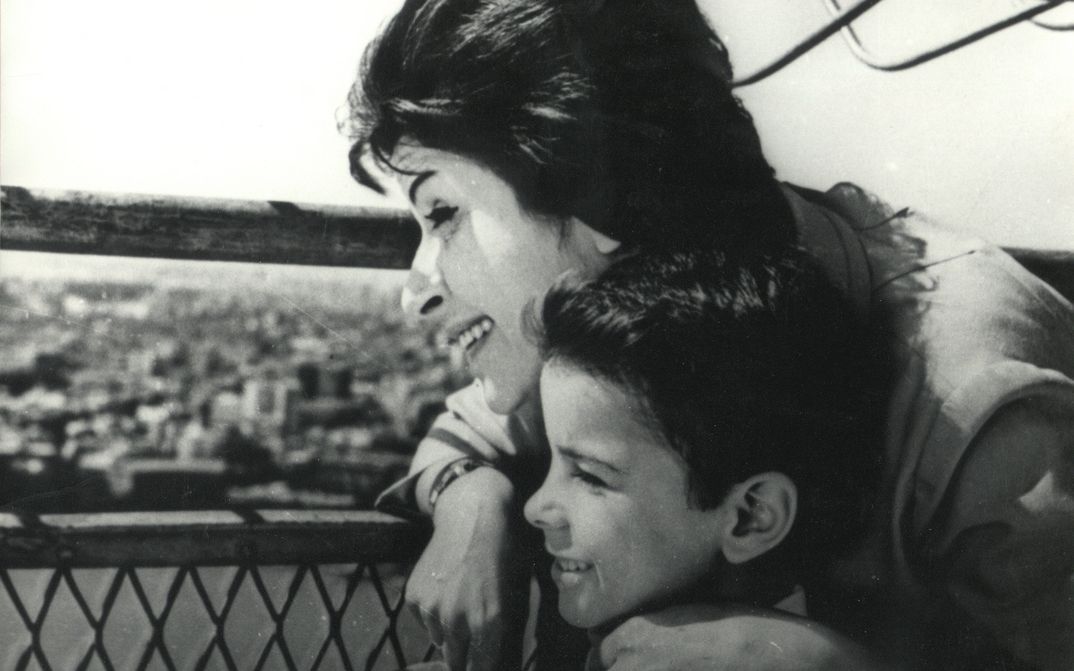Film still from DAWN OF A NEW DAY: A woman and a boy stand close together on a roof and look out over the city.