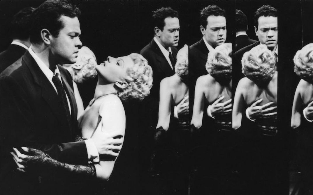 Filmstill aus THE LADY FROM SHANGHAI: Ein Mann hält eine Frau in den Armen, sie neigt ihren Kopf nach hinten. Sie sind in einem Spiegelkabinett und mehrfach gespiegelt.