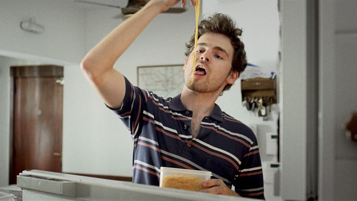 Filmstill from the movie "Arturo a los 30" by Martín Shanly. A young man is eating noodles from a tupperware with his hands.