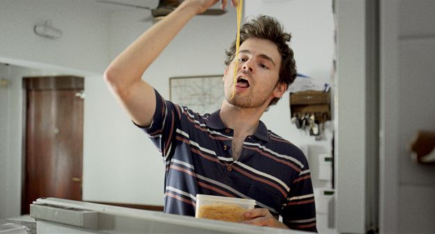 Filmstill from the movie "Arturo a los 30" by Martín Shanly. A young man is eating noodles from a tupperware with his hands.