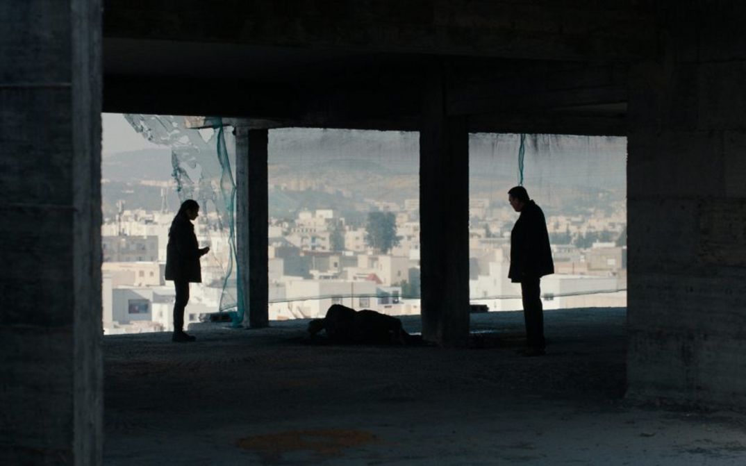 Film still from ASHKAL: Two people stand in a shell of a building, in the background you can see the city of Tunis.