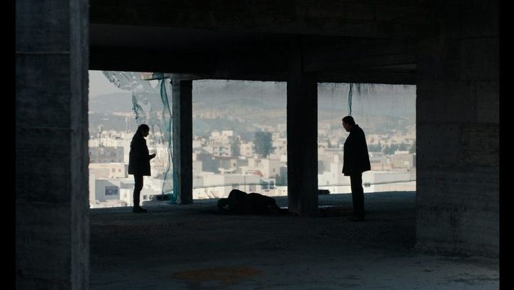 Film still from ASHKAL: Two people stand in a shell of a building, in the background you can see the city of Tunis.