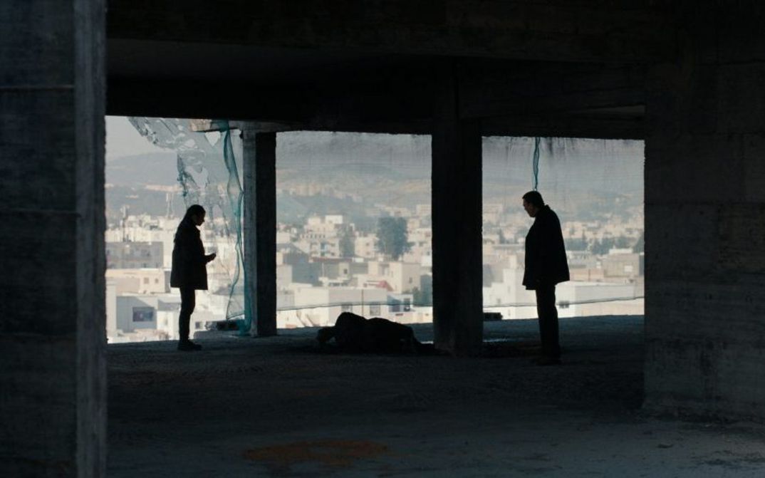 Filmstill aus ASHKAL: Zwei Personen stehen in einem Rohbau, im Hintergrund sieht man die Stadt Tunis.