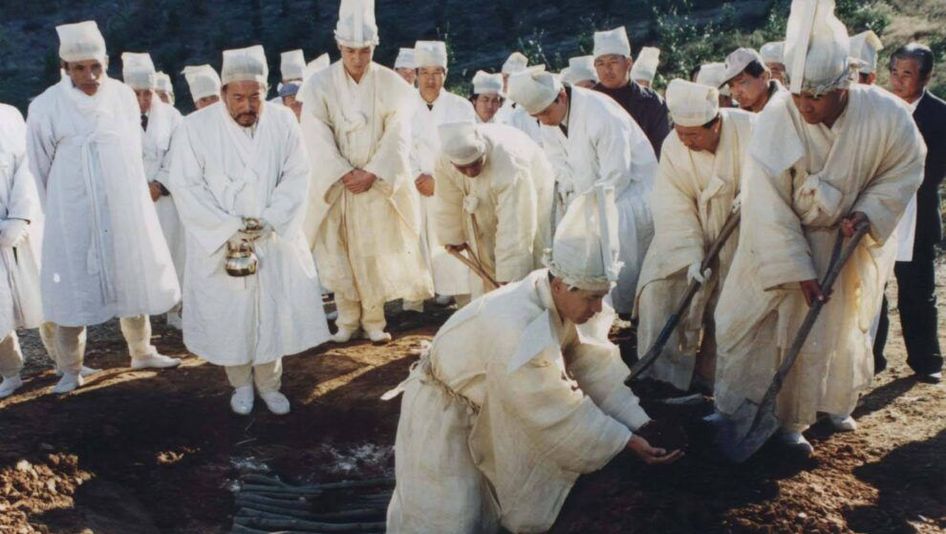 Filmstill aus FESTIVAL: Eine Gruppe von Männern in weißer Kleidung hebt ein Grab aus.