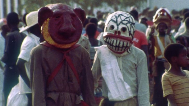 Film still from XARAASI XANNE – CROSSING VOICES: o people in masks in the middle of a crowd.