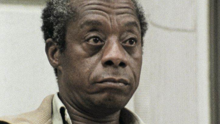Filmstill aus dem Film "I Heard It through the Grapevine" von Dick Fontaine. James Baldwin, ein älterer Mann mit grau-braunen Haaren und einer braunen Jacke, guckt unbeeindruckt rechts neben der Kamera vorbei.